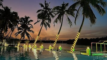 Una piscina con palmeras y un atardecer de fondo.
