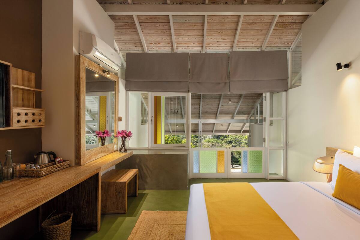 Un dormitorio con una cama grande, un escritorio de madera, un espejo y una ventana con vistas a zonas verdes.