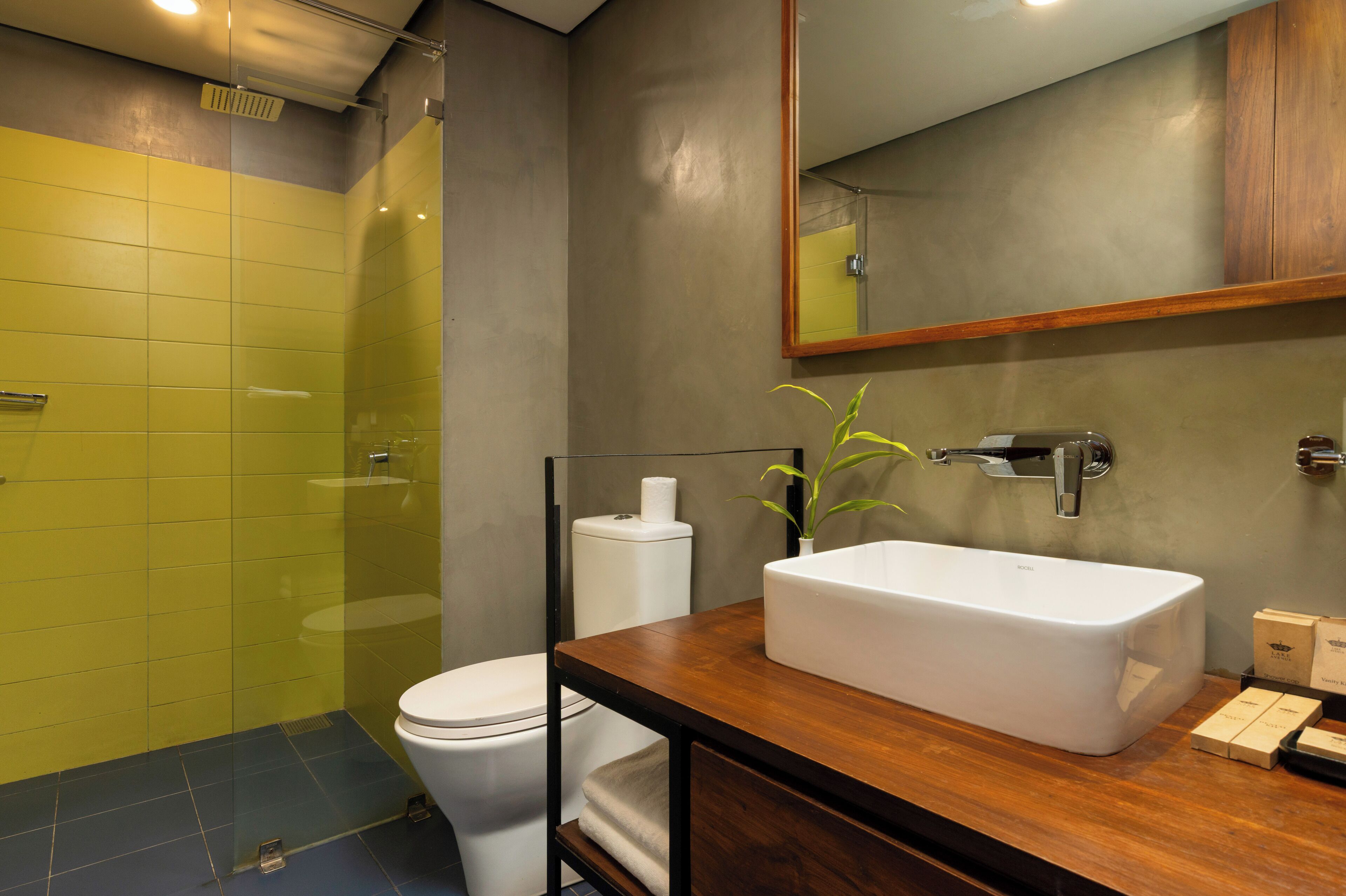 A modern bathroom with a glass shower enclosure, a white toilet, and a wooden vanity with a large sink.