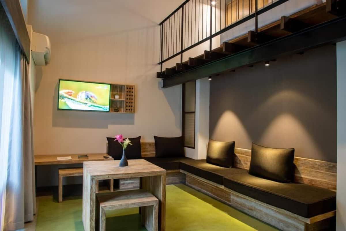 Una sala de estar moderna con un banco de madera, una mesita con un florero y un televisor de pantalla plana grande montado en la pared.