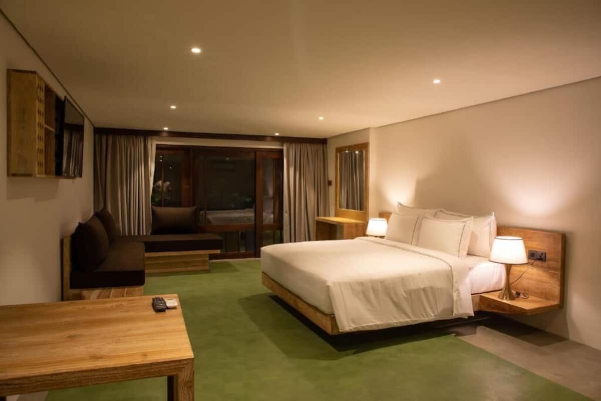 Habitación de hotel con cama, mesitas de noche, escritorio, silla y vista a través de un ventanal.