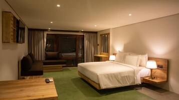 A hotel room with a bed, bedside tables, a desk, a chair, and a view through a glass door.