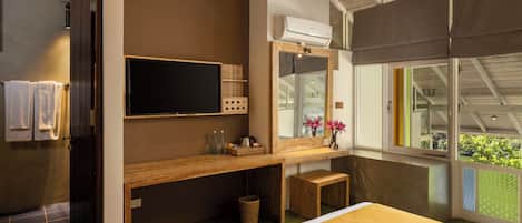 A modern hotel room with a large bed, a wooden vanity, a flat-screen TV, a large mirror, and a window with a view of greenery.