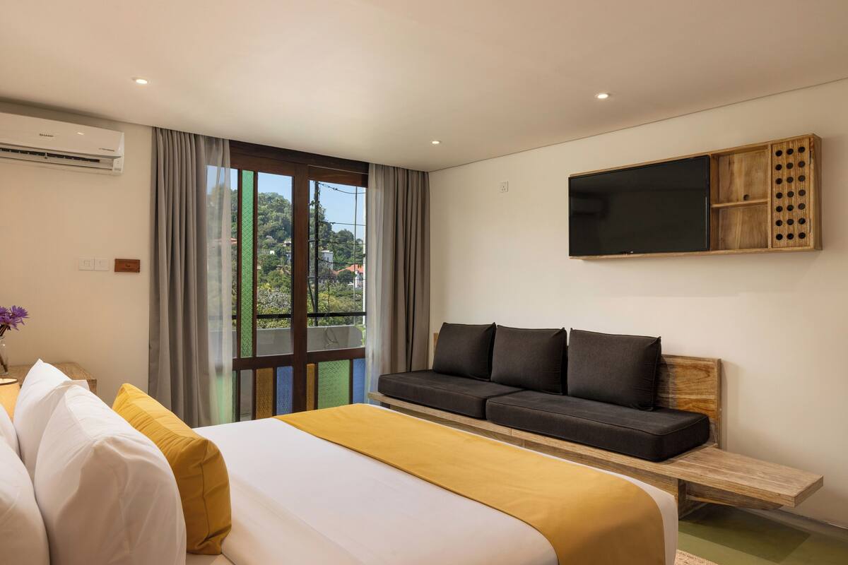 Habitación de hotel con una cama grande, un sofá, un televisor montado en la pared y vistas a zonas verdes.