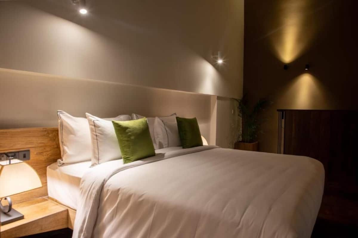 Una cama bien hecha con almohadas blancas y verdes, un cabecero de madera y una lámpara de noche.