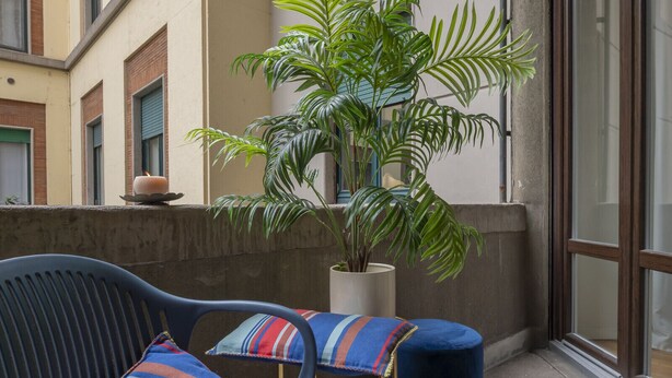 A balcony with a blue chair, a striped cushion, a potted plant, and a small table with a candle.