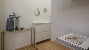 A minimalist room with a wooden floor, a white cabinet, a glass console table with decorative items, and a book titled "INGRESSI DI MILANO" on a wooden table.