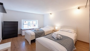 A hotel room with two beds, a window with a view, a black dresser, and a white desk. - Beautiful House In Porta Soprana Genova (Genoa)