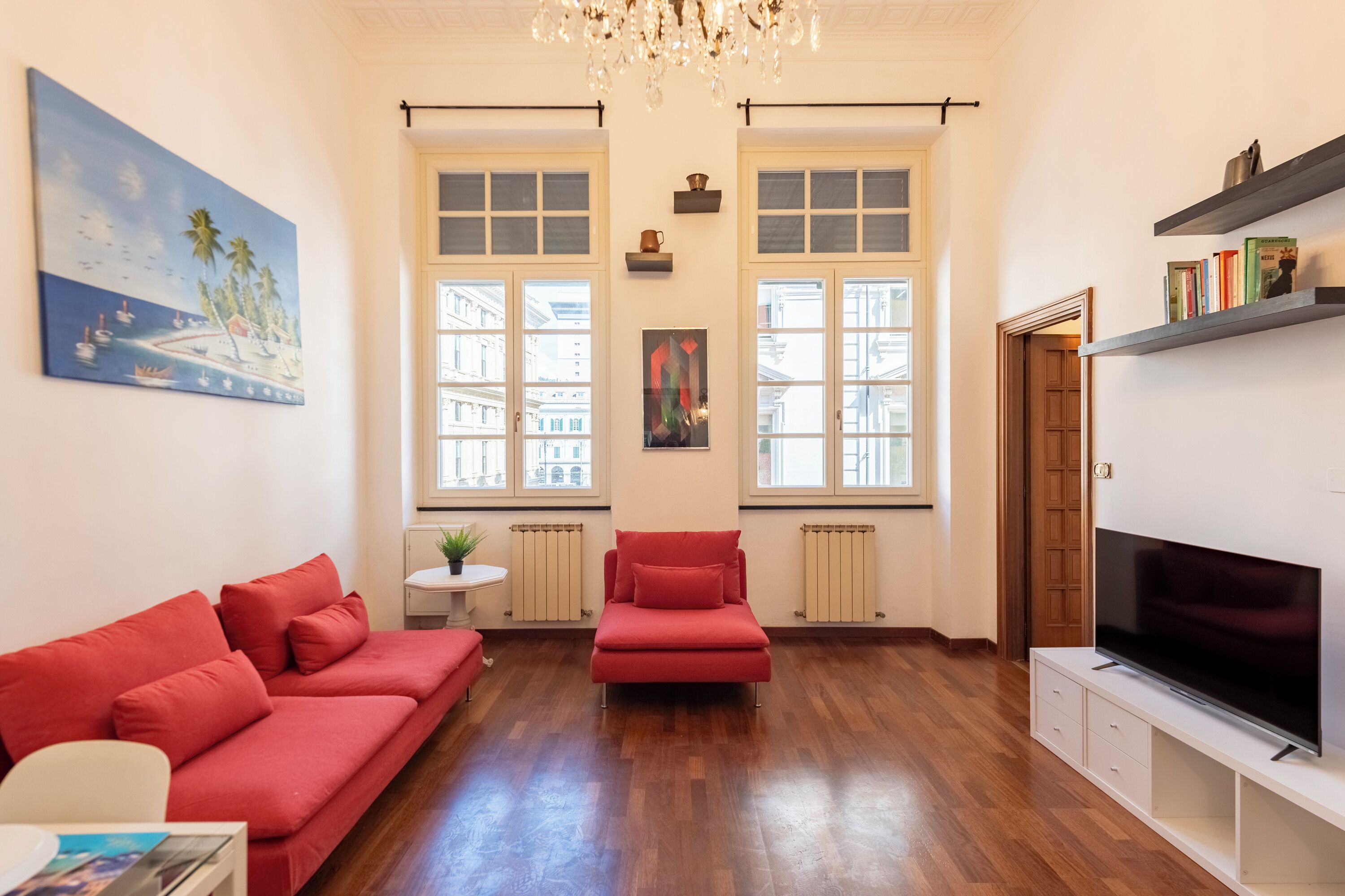 A living room with a red sofa, a red armchair, a TV, and a bookshelf.