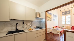 A modern kitchen with a sink, stove, and cabinets. There is a dining area with a table and chairs. - Beautiful House In Porta Soprana Genova (Genoa)