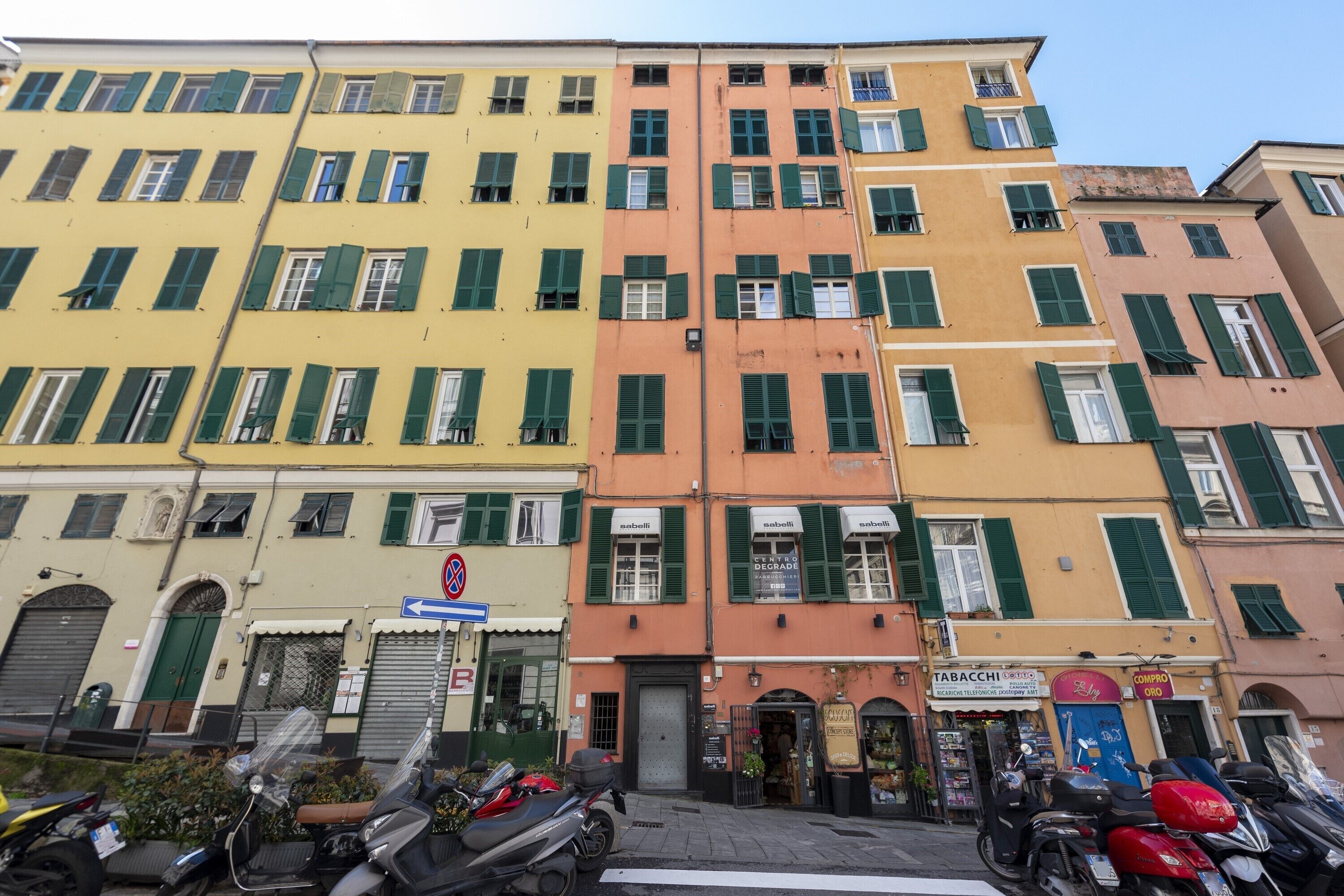A row of colorful buildings with green shutters, a visible storefront, and parked motorcycles.
