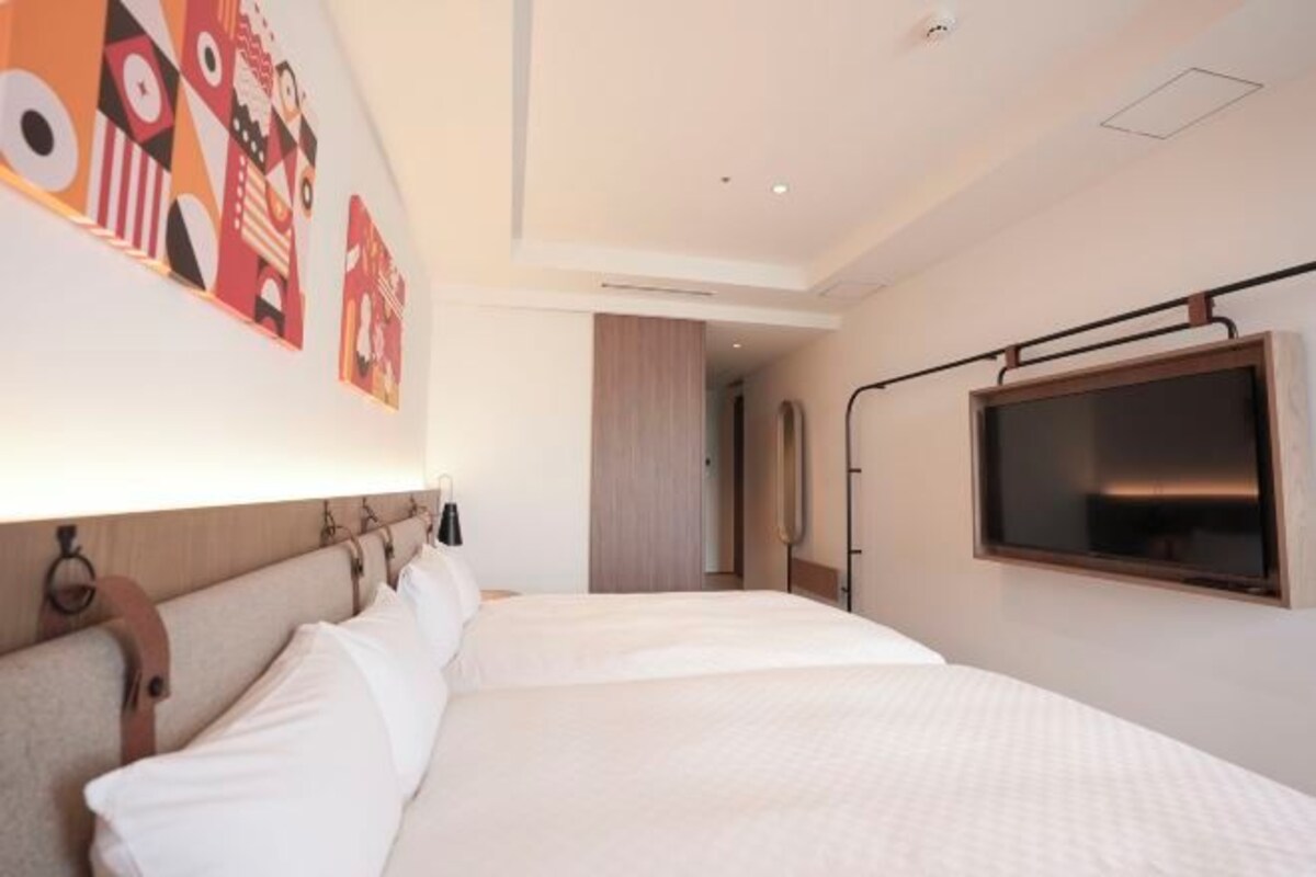 A modern hotel room with a large bed, a flat-screen TV mounted on the wall, and abstract artwork above the bed.
