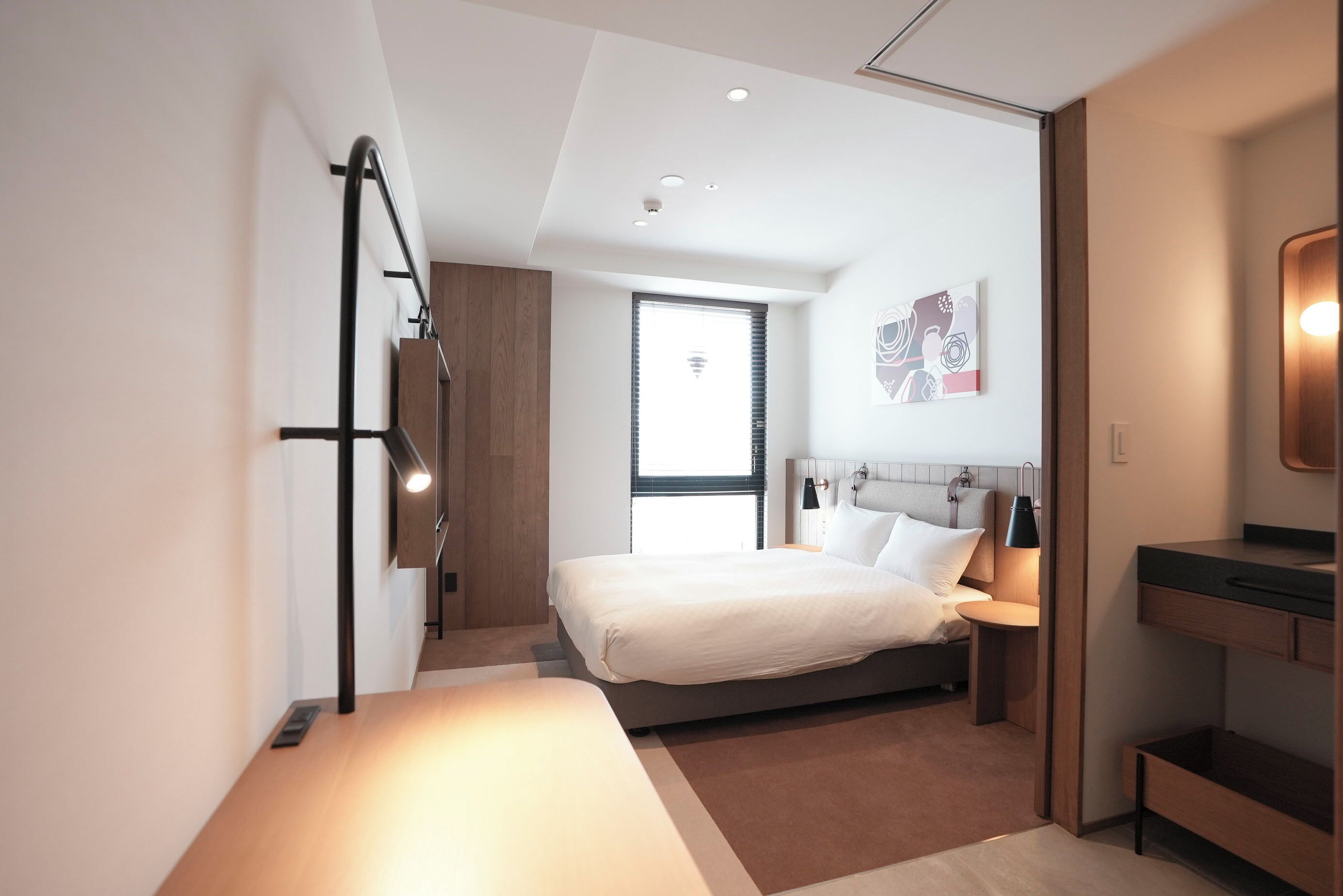 A modern hotel room with a bed, bedside table, and a large window.