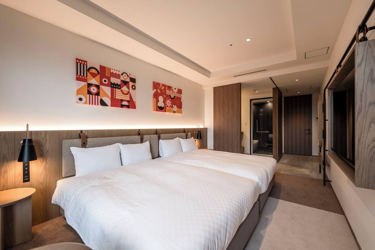 Quarto de hotel moderno com uma cama grande, mesa de cabeceira, luminária e arte abstrata.