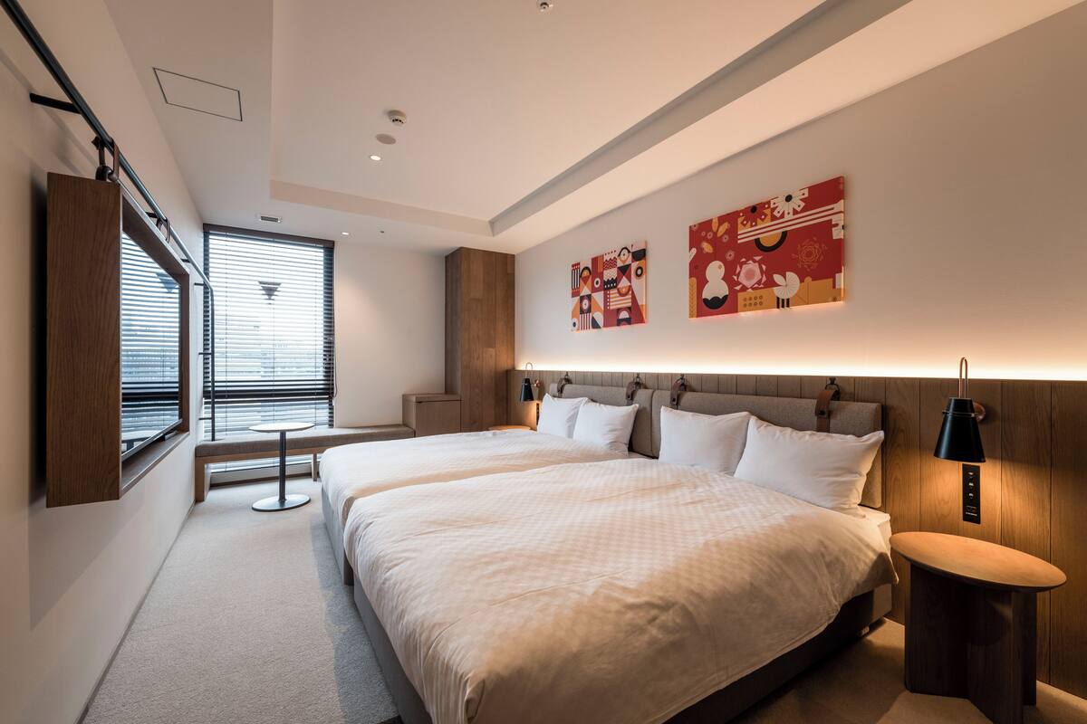 Quarto de hotel moderno com duas camas, uma mesa pequena e obras de arte nas paredes.