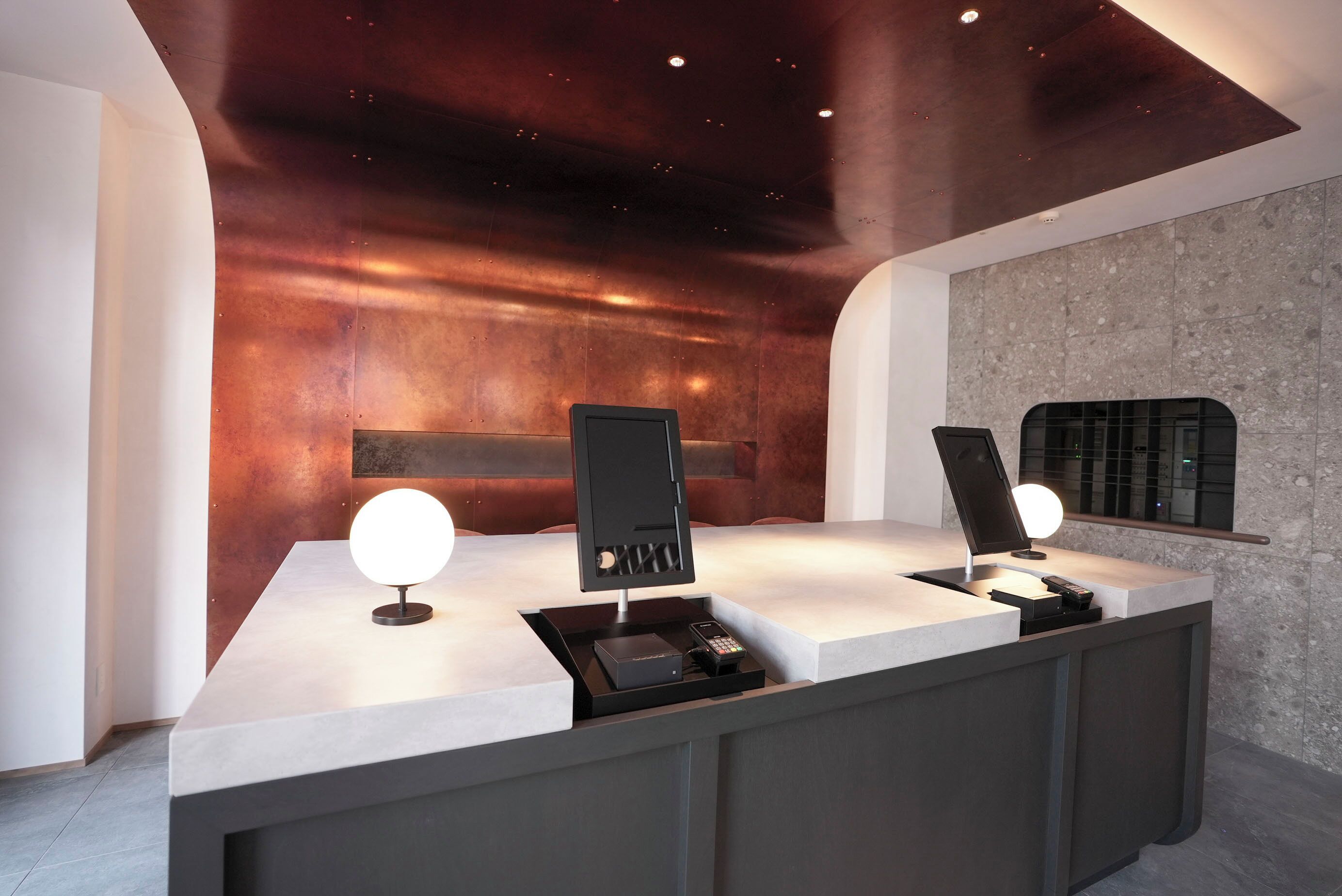 Un mostrador de recepción moderno con un diseño elegante, que incluye una pared metálica y una pared decorativa con textura de piedra.