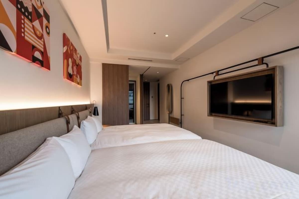 A hotel room with a large bed, a flat-screen TV mounted on the wall, and a door leading to a hallway.