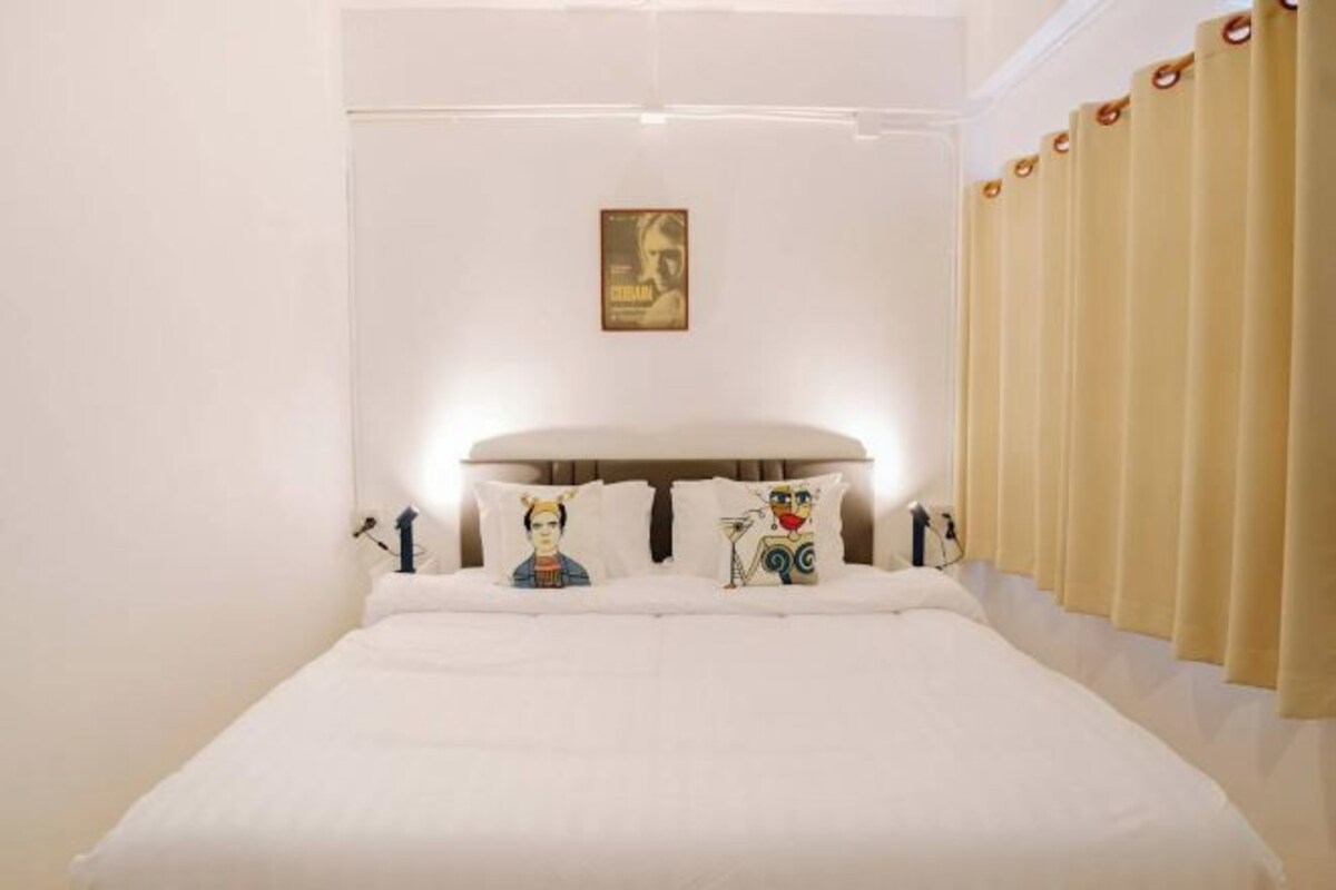 Une chambre d’hôtel avec un grand lit, du linge de lit blanc et une tête de lit agrémentée de coussins décoratifs.
