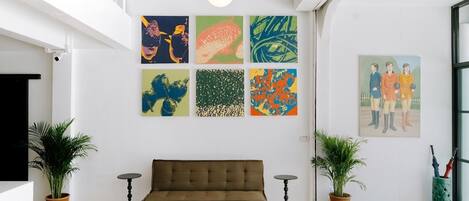 Un intérieur moderne avec un canapé marron, deux plantes en pot et une série de peintures abstraites aux couleurs vives accrochées au mur.