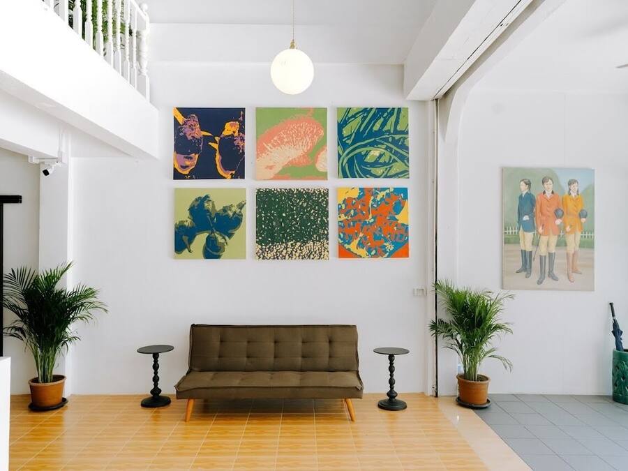 A modern interior with a brown sofa, two potted plants, and a series of colorful abstract paintings on the wall.