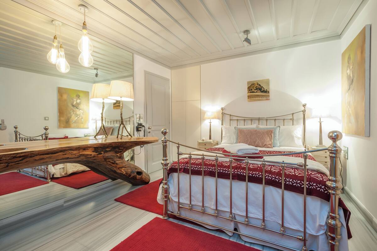 Un dormitorio con cabecera de madera, cama con estructura de metal, un espejo grande y una alfombra roja.