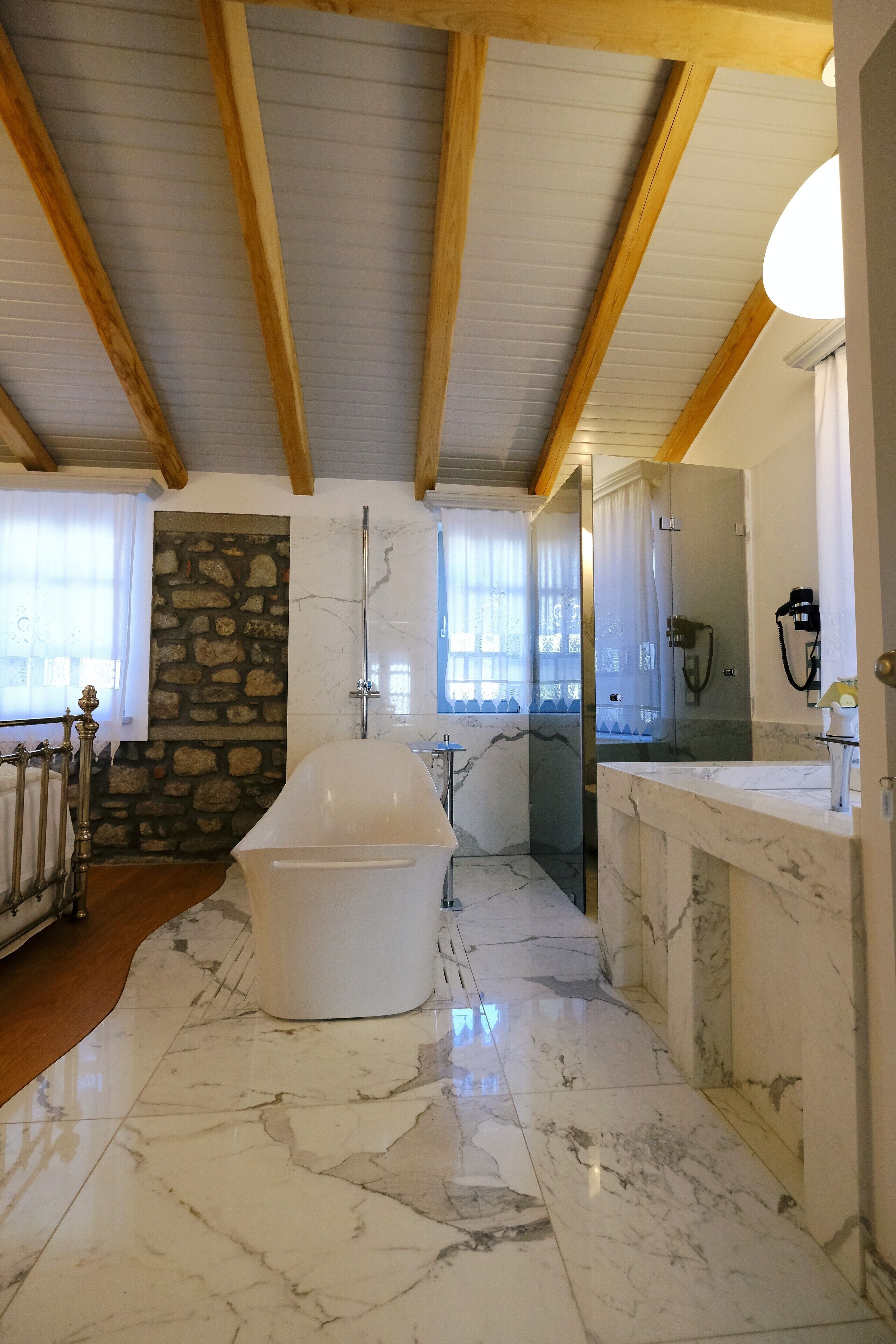 Une salle de bain avec un sol en marbre, une baignoire sur pieds, un mur en pierre et un plafond en bois.