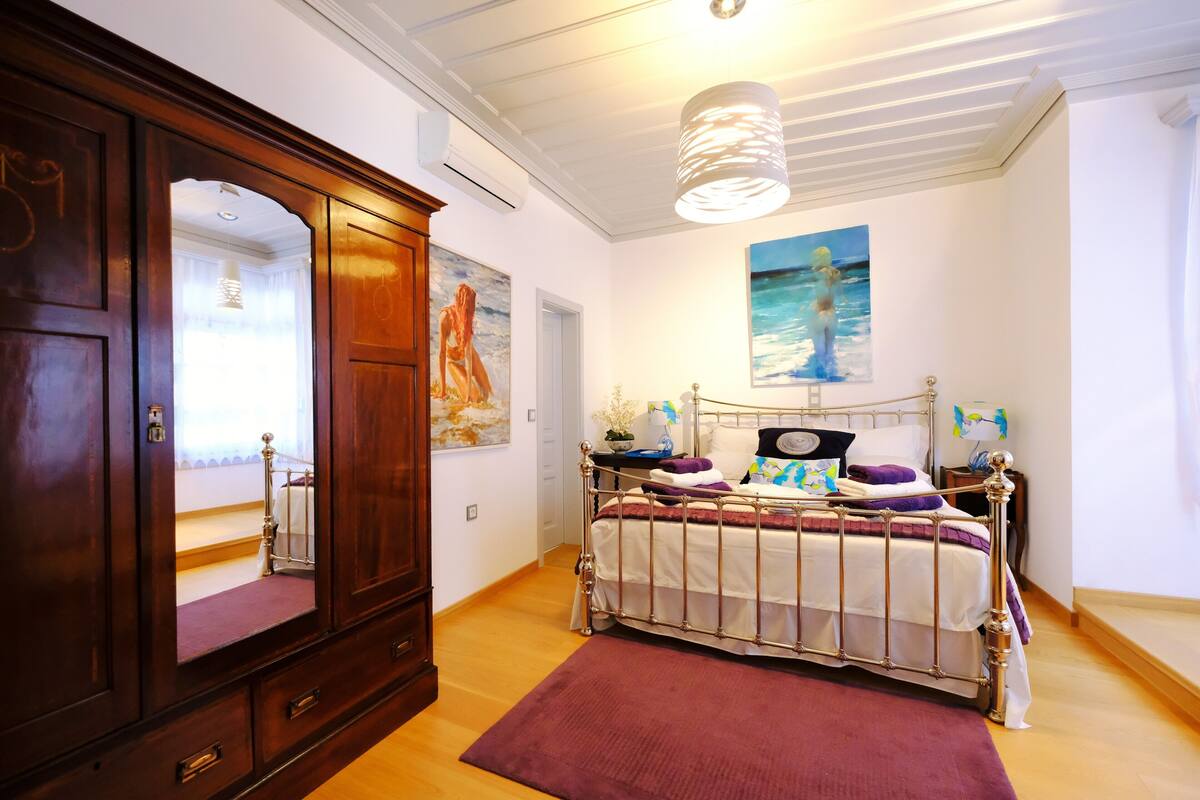 Un dormitorio con un armario de madera, una estructura de cama metálica, un espejo grande y un cuadro de una mujer en la pared.
