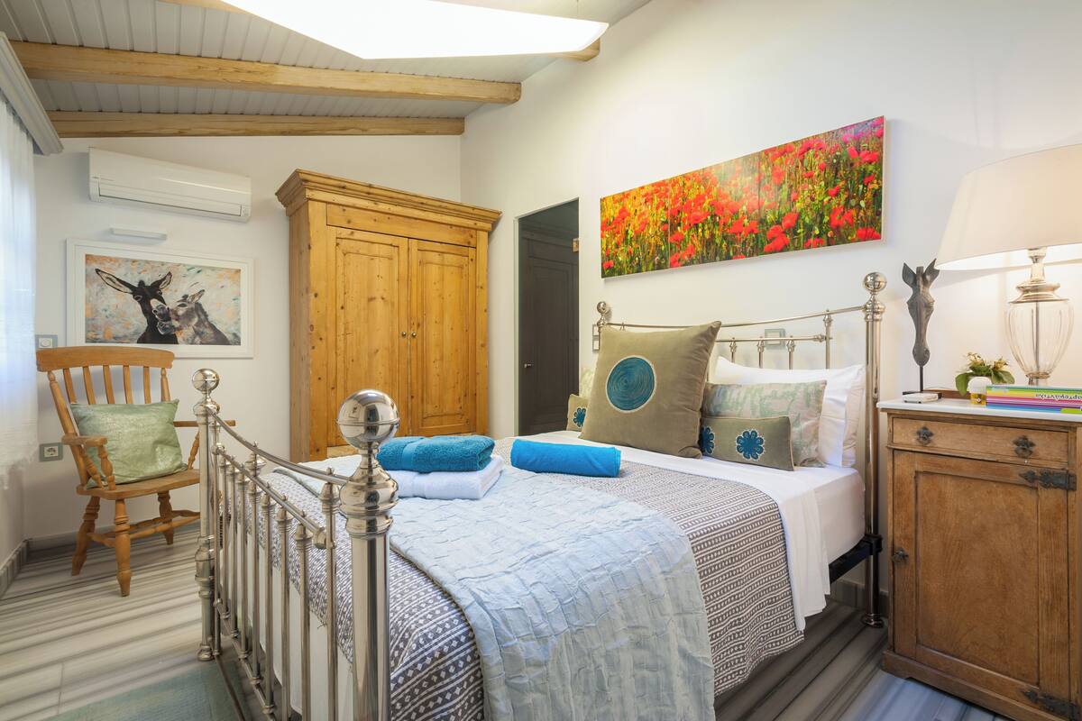 Un dormitorio con cama, un armario de madera, una silla, un cuadro y una lámpara.