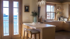 Uma cozinha com uma ilha grande, banquetas de bar, vista para o mar pelas portas de correr e um lustre pendurado.