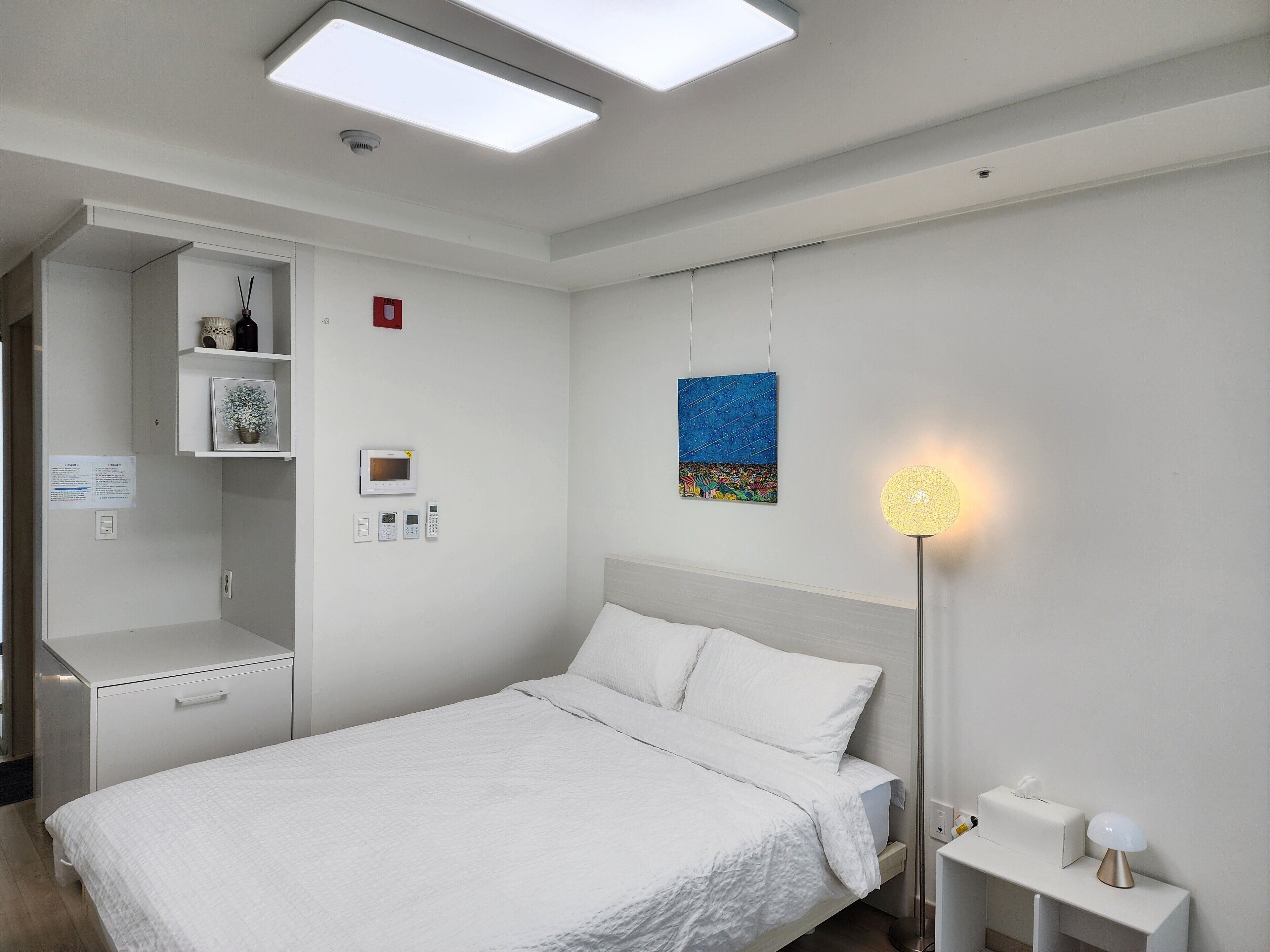 A modern bedroom with a bed, bedside table, lamp, and a wall-mounted shelf with decorative items.