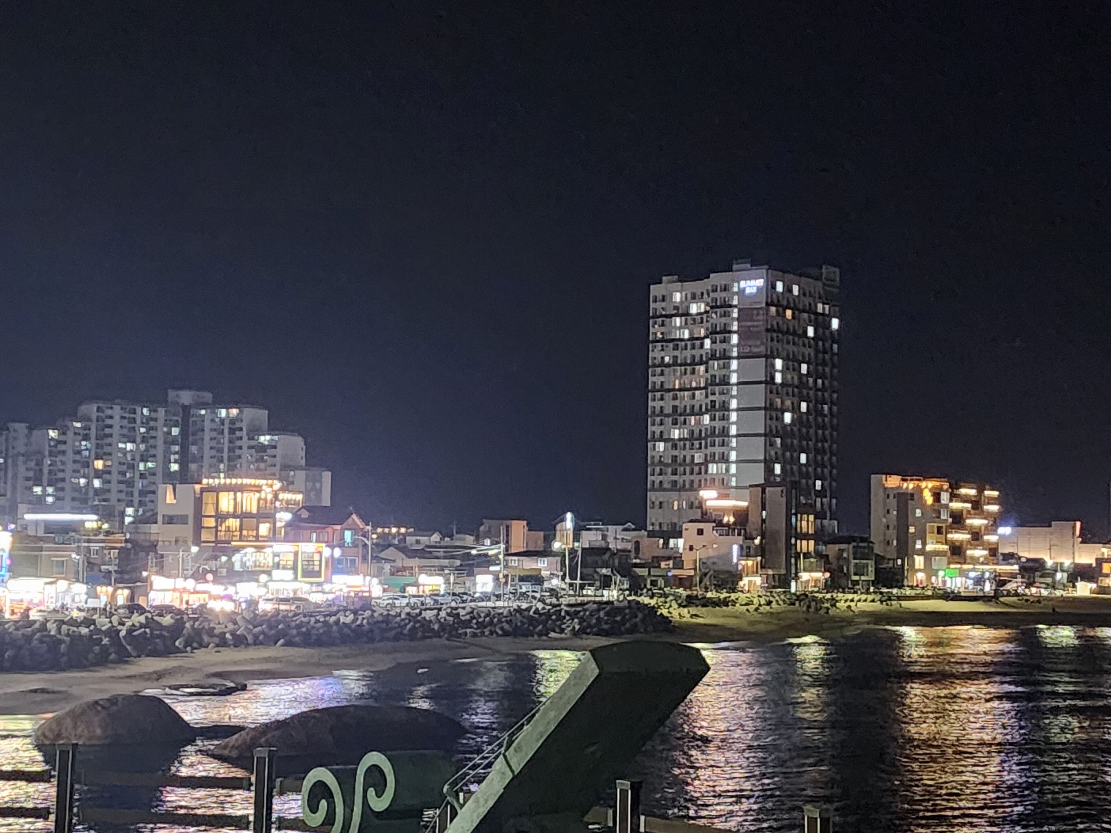 A nighttime cityscape with illuminated buildings and a waterfront.