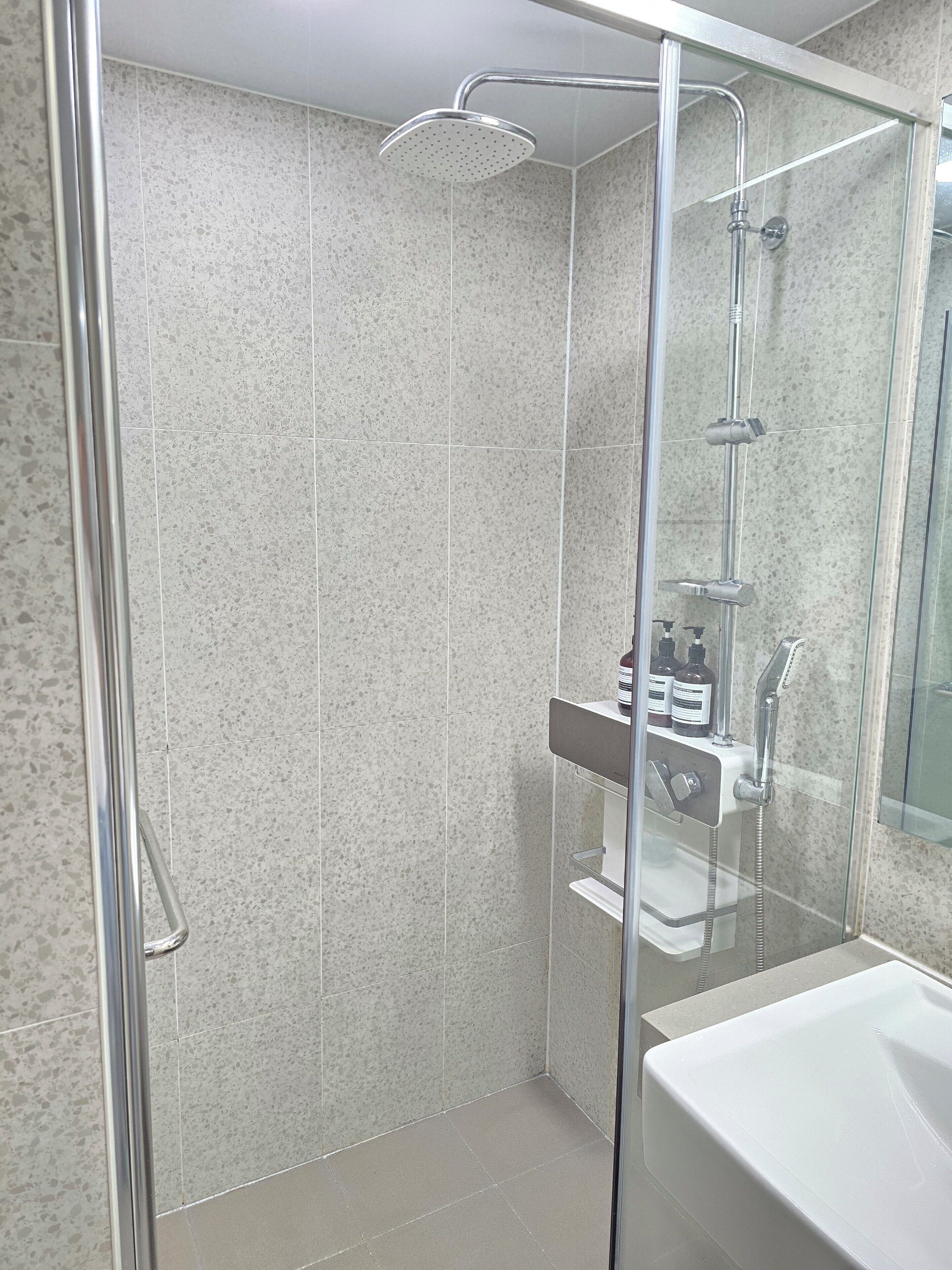 A modern bathroom with a glass-enclosed shower, a white sink, and a shelf with toiletries.