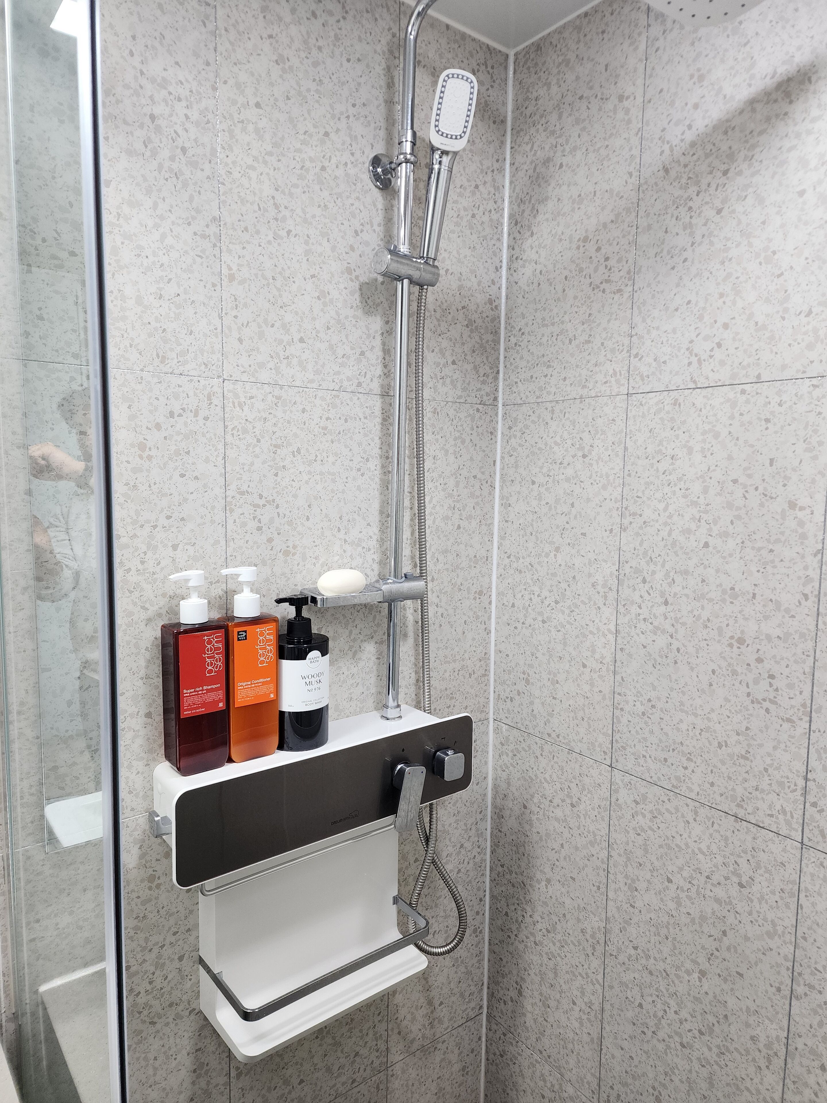A shower area with a handheld showerhead, a glass door, and a shelf with toiletries.