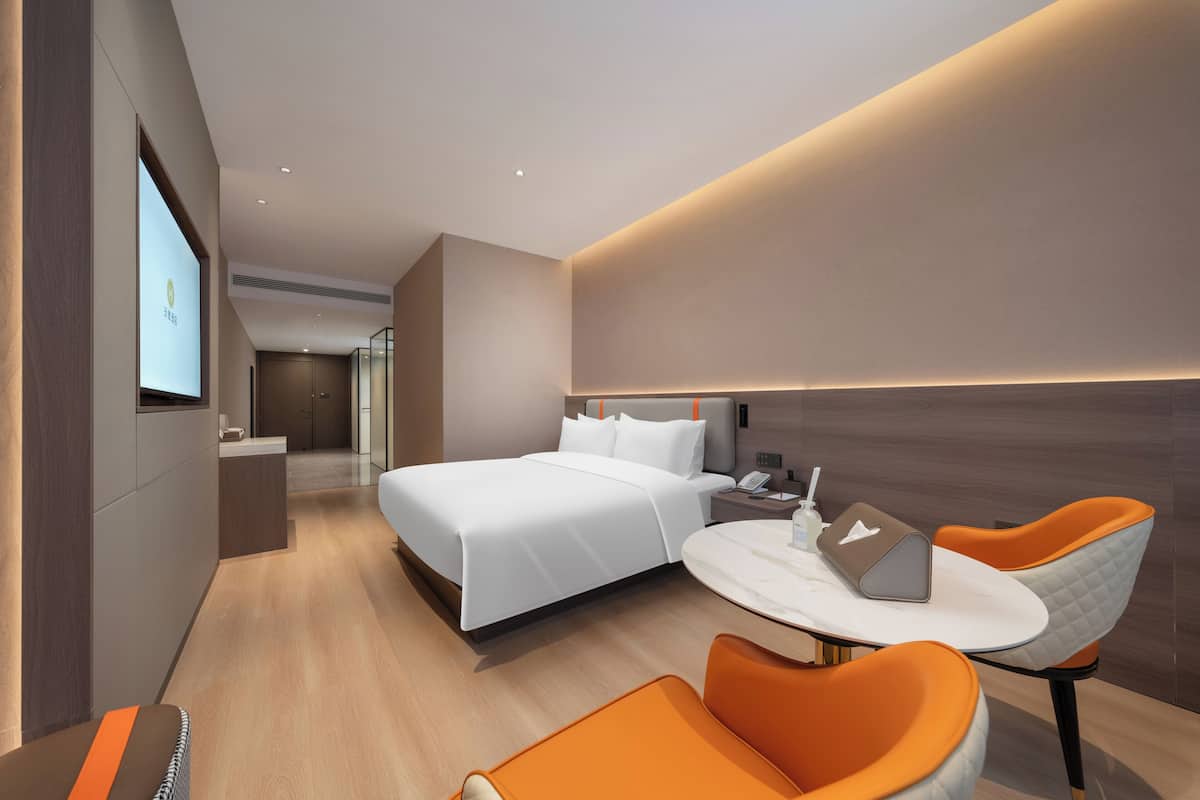 Ein modernes Hotelzimmer mit einem großen Bett, einem Schreibtisch mit einem Laptop und zwei orangenen Sesseln.