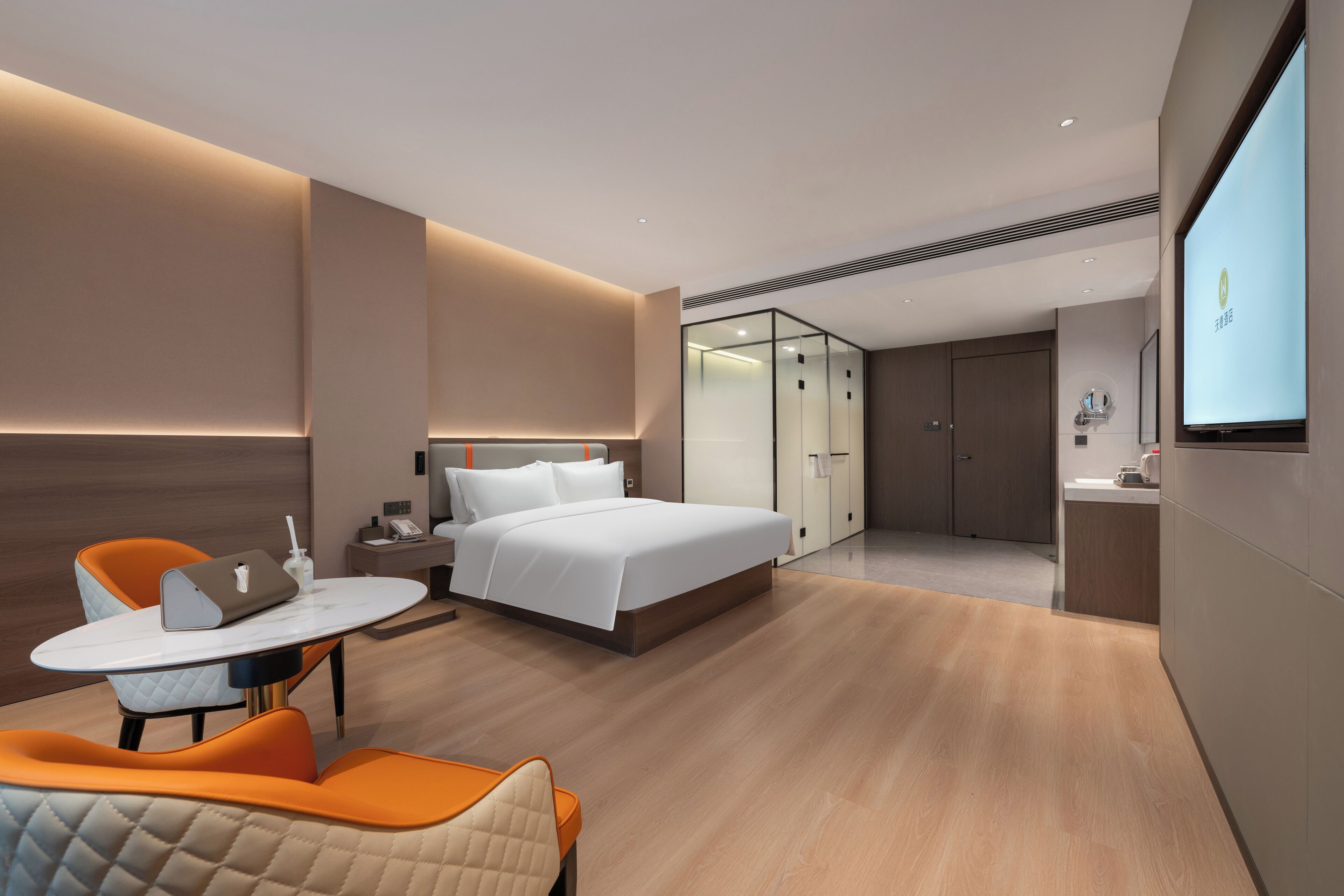 A modern hotel room with a bed, a desk with a laptop, a chair, and a TV screen.