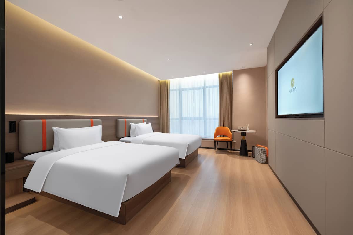 Ein modernes Hotelzimmer mit zwei Betten, einer Sitzecke und einem großen Bildschirm an der Wand.