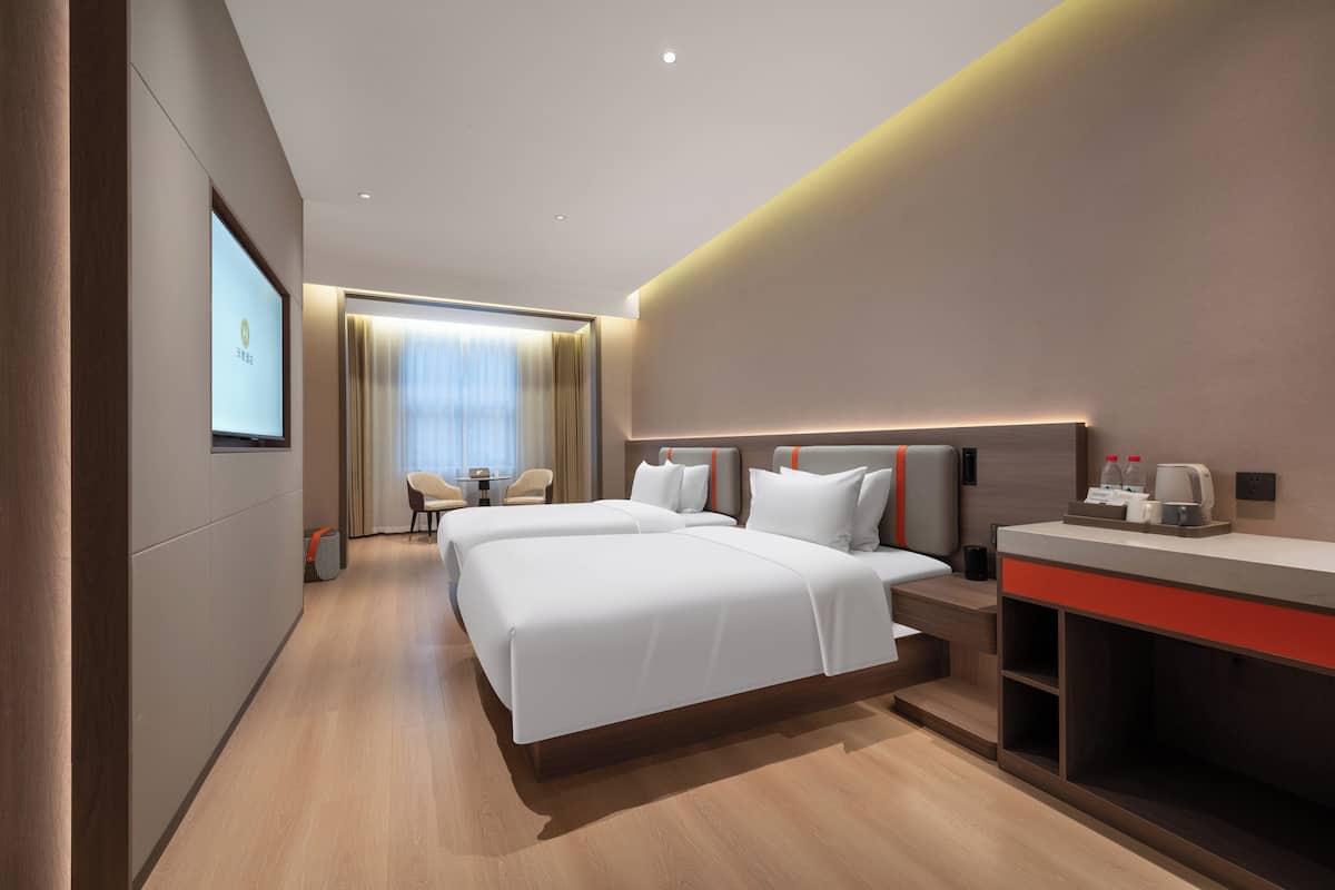 Ein modernes Hotelzimmer mit einem großen Bett, einem Schreibtisch mit Kaffeemaschine und einem an der Wand montierten Fernseher.