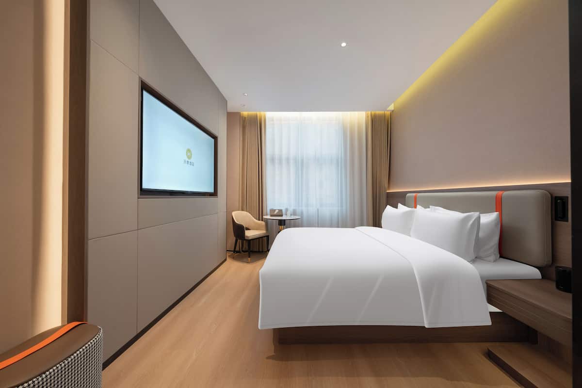 Ein modernes Hotelzimmer mit einem großen Bett, einem an der Wand befestigten Fernseher, einem kleinen Tisch und einem Stuhl.