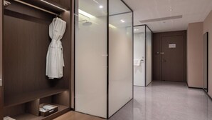 A modern hotel room with a wooden wardrobe, a glass partition, and a robe hanging on the door. - World Hotel Hualian Shoppin Plaza branch (Kaifeng)
