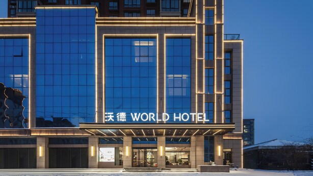 A modern hotel with a large glass facade and illuminated signage. - World Hotel Hualian Shoppin Plaza branch (Kaifeng)