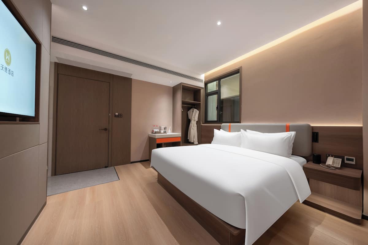 Ein modernes Hotelzimmer mit einem großen Bett, einem Nachttisch mit Telefon, einem Spiegel und einem Kleiderschrank.