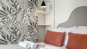 Ein ordentlich bezogenes Bett mit weißen und braunen Kissen, einem grauen Kopfteil und einer Wand mit einem Farnblattmuster.