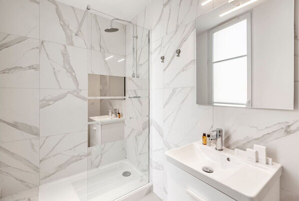 A modern bathroom with a glass shower enclosure, a white sink with a mirror, and marble-patterned walls.