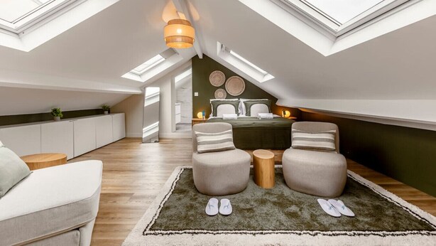 A modern loft bedroom with skylights, a bed, a seating area, and a kitchen.