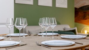A dining table set with clear glasses, plates, and cutlery, with a green wall and artwork in the background.