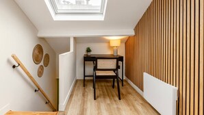 A room with a skylight, a wooden floor, a table with a lamp, and a wall with vertical wooden slats.