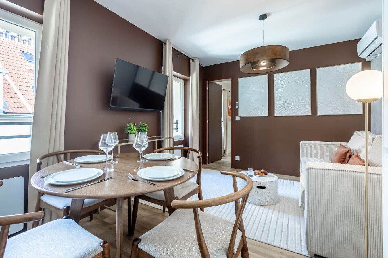 A modern hotel room with a dining area, a flat-screen TV mounted on the wall, and a cozy seating area with a sofa and armchairs.