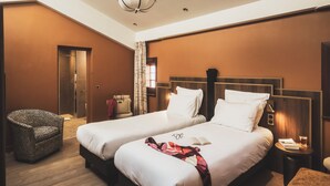 A hotel room with two beds, a sitting area with a chair, a small table, and a nightstand. - Parc Victoria Appartements (Saint-Jean-de-Luz)