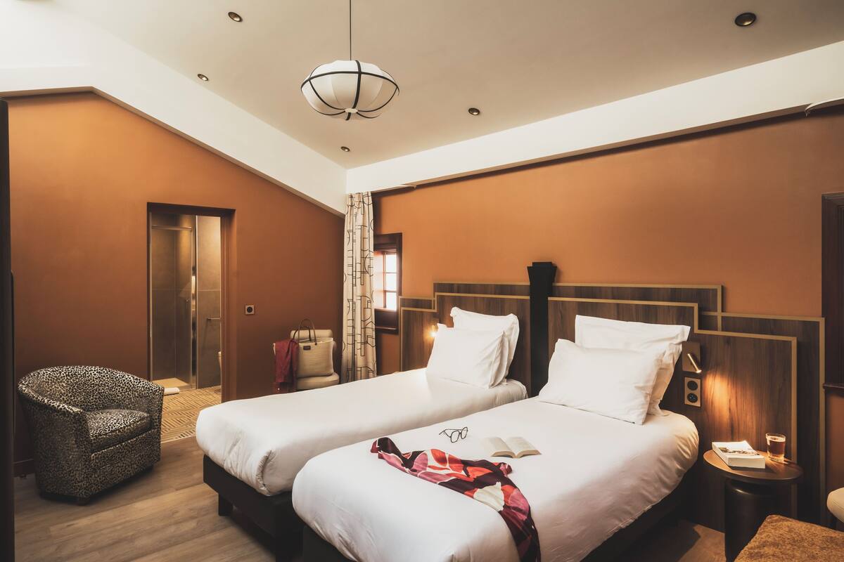 A hotel room with two beds, a sitting area with a chair, a small table, and a nightstand.