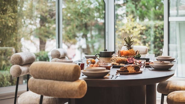 A dining table with breakfast items and chairs in a room with large windows and a view of greenery. - Parc Victoria Appartements (Saint-Jean-de-Luz)